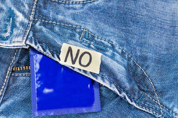 Inscription NO on torn paper and condom in foil blue package on new jeans