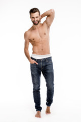 Fototapeta premium Cheerful handsome man. Full length of handsome young man in jeans looking at camera with smile while standing against white background.