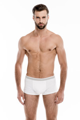 Confident and sexy. Handsome shirtless young man in white pants looking at camera while standing against white background.