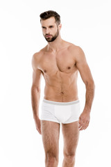 Handsome and muscular. Handsome shirtless young man in white pants looking away while standing against white background.