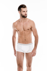 Fototapeta premium Muscular and healthy. Handsome shirtless young man in white pants looking away while standing against white background.