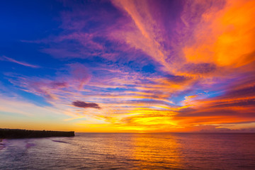 Silhouette of a cliff against the background of an colorful sunset. Sea waves break on the rocks. Sunset on Jimbaran, South Kuta, Bali, Indonesia.