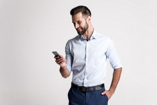Great email! Handsome young man using his phone with smile while standing against white background.