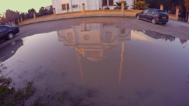 a reflection of a modern mosque in a large puddle of water in the city of Famagusta