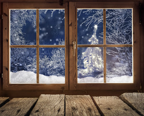 Blick aus einer Holzhütte auf einen Winterwald mit Weihnachtsbaum am Abend