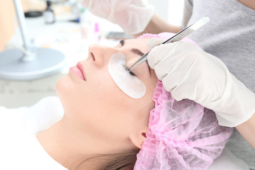 Naklejka premium Young woman undergoing eyelash extensions in beauty salon