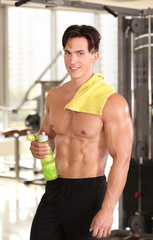 Muscular young man with bottle of water in gym