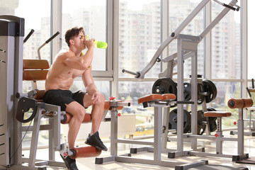 Obraz na płótnie Canvas Muscular young man drinking water in gym