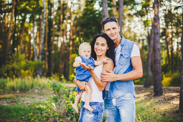 Fototapeta premium stylish beautiful fashionable parents are holding a girl in the park on the background of a dense forest.