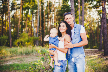 Fototapeta premium stylish beautiful fashionable parents are holding a girl in the park on the background of a dense forest.