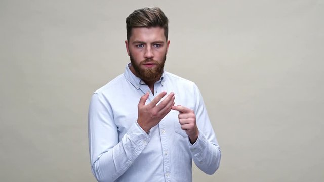 Thoughtful bearded man in shirt recounts something on fingers over gray background