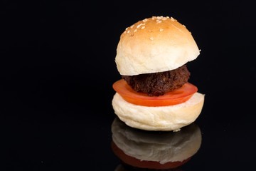 Meat ball with tomato in sliced bun isolated above black background with reflections