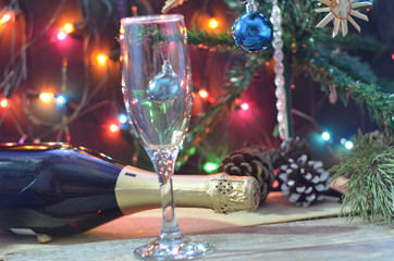 a bottle of champagne and glasses on the background of a Christmas tree decorated with balls and New Year's lights. happy christmas concept. Ribbon, baubles and wine against Christmas lights