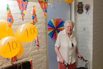 senior woman stands in front of her decorated room door celebrating her 100th birthday