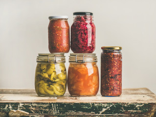 Autumn seasonal pickled or fermented colorful vegetables in glass jars over vintage kitchen drawer, white wall background, copy space. Fall home food preserving or canning