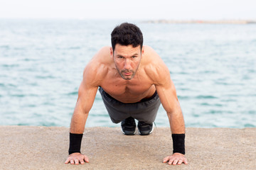 Athletic man making push ups by the sea