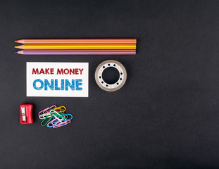 make money online. Top view of a black ofice desk. Colored pencils, business card and adhesive tape.