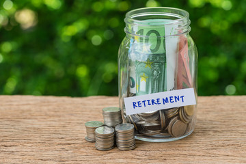 glass jar bottle labeled as retirement with full of coins and banknotes as savings or investing for retirement concept
