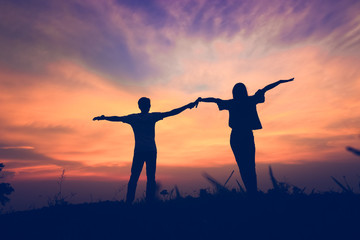 Fototapeta premium Couple holding hands with arms outstretched at sunset