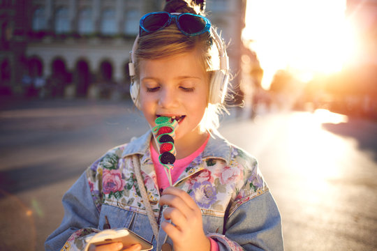 little girl  listening  music  and eating  fruit lollipop,beautiful sunset on urban street,