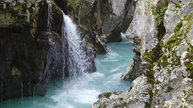 Small waterfall pouring into the Soca River in narrow canyon cut through the landscape in Slovenia.