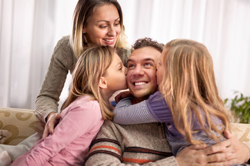 Obraz premium beautiful young parents and their cute little daughters, hugging smiling, Girl is kissing her dad