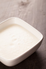 
Small bowl of white cheese sauce for dipping broccoli or vegetables on dark wooden background vertical shot
