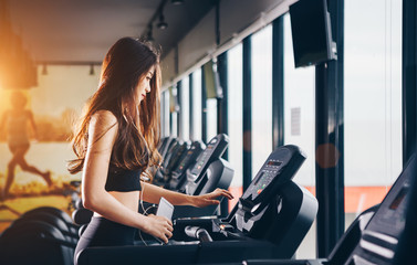 Obraz na płótnie Canvas Asian woman exercising in the gym, Young woman workout in fitness for her healthy and office girl lifestyle. She using smart phone to check an email or social network.
