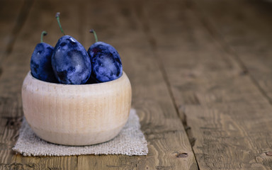 Wooden bowl with ripe plums on a piece of burlap on vintage table.