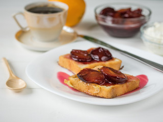 Two pieces of French bread with plum jam, with coffee, orange curd cream.