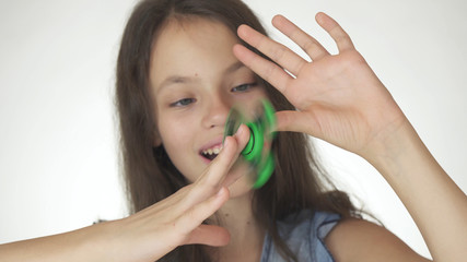 Beautiful cheerful teen girl playing with green fidget spinner on white background