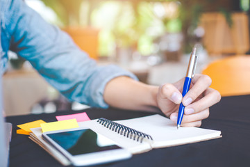 Woman hand is writing on notepad with a pen in the office.