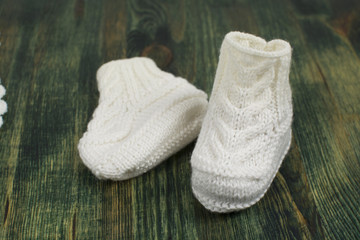 Baby white knitted socks booties, on a background of green painted wood.