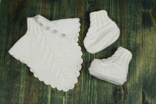 White knitted baby socks, booties, and jacket on a background of green painted wood.