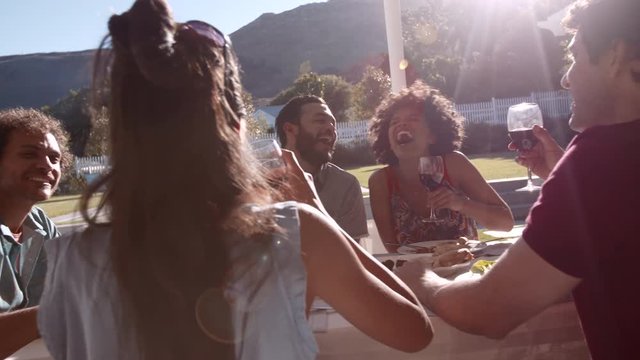 Group of happy young friends sitting around a table and having wine. Young people having drinks during outdoor lunch.