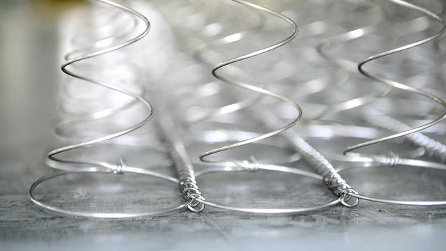 plant for making mattresses. Independent metal springs are fixed on rings and move. New curved products are joined together in even rows and at the same interval.