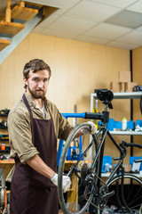 Fototapeta na wymiar Confident repairman in uniform tightening gear of bicycle wheel