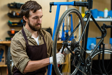 Master in apron fixing cogwheel of bike during working day