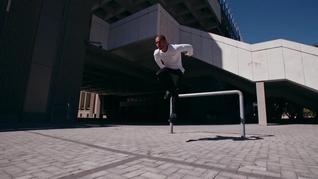 Man jumping over a railing and practices parkour outdoors. Male free runner performing parkour in urban space.