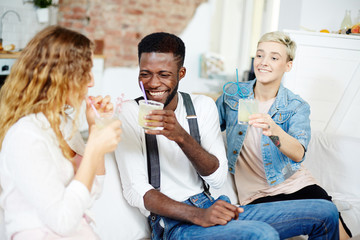 Laughing guy with cocktail talking to one of girls during home party