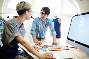 Two young fashion designers consulting about dress models and fabric for new collection
