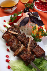 Kebab of mutton ribs marinated in wine.Red bell pepper,cumin,coriander seeds,salt to taste.Served with chopped onions and herbs,a sprinkle of vinegar.Uzbek cuisine.The upper projection.