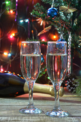 a bottle of champagne and glasses on the background of a Christmas tree decorated with balls and New Year's lights. happy christmas concept. Ribbon, baubles and wine against Christmas lights