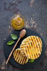 Above view of grilled pineapple slices with addition of honey served on a stone slate tray, brown stone background with space