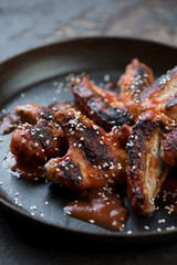 Closeup of grilled chicken wings served with sauce and sesame seeds, selective focus, shallow depth of field