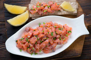 White fish-shaped plate with salmon tartar and bread slices in a rustic wooden setting, top view