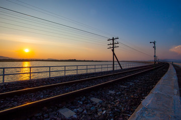 Fototapeta na wymiar rail way track over water reservoir and beautiful sun set sky