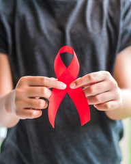 Aids red ribbon on girl teenager’s hand support for World aids day and national HIV/AIDS awareness month campaign concept