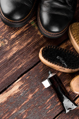 Black boots on wooden background with polishing equipment, brush and polish cream. Top view.  Flat lay