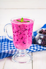 Smoothies of black currant in a glass with a handle on a white wooden table.